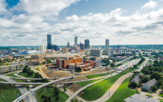 The city skyline of Tulsa, OK is surrounded by highways with cars driving in multiple directions